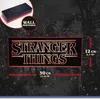 A promotional image for a Stranger Things logo light, showing its dimensions and a wall-mountable feature. Produktbild-Vorschau
