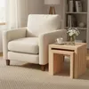 A cream-colored armchair is placed next to a set of nesting side tables. A vase of daisies and a cup of tea are on the top table. Produktbild-Vorschau