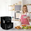 A woman in a kitchen is looking at a tablet while an air fryer and fresh vegetables are on the counter. Produktbild-Vorschau