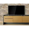 A modern living room setup with a television on a wooden media console against a stone-tiled wall. Produktbild-Vorschau