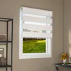 A white zebra roller blind is installed on a window, with a view of a green lawn and trees outside. Voir les images du produit