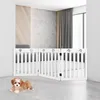A small dog is lying on the floor in front of a white wooden pet gate set up in a modern room with a window and curtains in the background. Produktbild-Vorschau