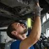 A mechanic is working on the underside of a car, illuminated by a work light. Voir les images du produit