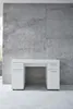 A white desk with drawers against a textured concrete wall. Produktbild-Vorschau