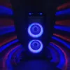 A tall speaker with two illuminated blue drivers is shown in a dark room with streaks of red and blue light on either side. Voir les images du produit
