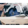 A close-up shot of a person using a Bosch circular saw to cut a piece of wood. Sawdust is flying. Produktbild-Vorschau