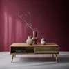 A wooden coffee table with decorative vases and books on it, set against a deep pink wall with light shadows. Produktbild-Vorschau