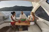 Three people are enjoying a meal on a yacht with a scenic view of a coastline and mountains in the background. Produktbild-Vorschau