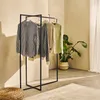 A clothing rack with several garments displayed in a room with a plant and a woven pouf. Produktbild-Vorschau