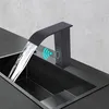 A black waterfall faucet with a sensor is shown in use over a black sink. Podgląd zdjęcia produktu