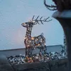 A lighted wire reindeer decoration sits on gravel in front of a white wall. Podgląd zdjęcia produktu