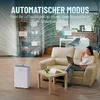 A woman is sitting on a couch using a laptop while a dehumidifier is in the foreground. Produktbild-Vorschau