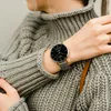 A person wearing a grey sweater and a smartwatch. Anteprima dell’immagine prodotto