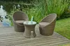 A wicker club set with two chairs and a table is placed on a wooden deck next to a body of water with reeds. Produktbild-Vorschau