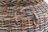 A close-up view of a woven basket handle made of multiple strands of rattan in various shades of brown and gray. Produktbild-Vorschau