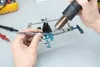 A close-up shot of a person's hands repairing a circuit board with a heat gun and tweezers. Produktbild-Vorschau