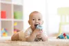 A baby is lying on a carpet and holding a baby bottle. Náhľad obrázku produktu