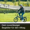 A man is riding an electric bicycle on a paved path in a park with green grass and trees in the background. Produktbild-Vorschau