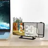 A digital alarm clock with a projector is placed on a wooden desk next to a laptop. Náhled obrázku produktu