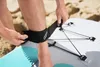 A person is securing a leash to their ankle while standing on a sandy beach next to a paddleboard. Produktbild-Vorschau