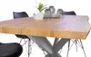 A close-up view of a wooden dining table with a metal spider leg base, set against a white background. Chairs are visible in the background. Produktbild-Vorschau
