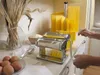 A person making pasta at home with a pasta maker and drying rack. Produktbild-Vorschau