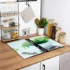 A kitchen counter with various items, including glass cutting boards with a nature design, jars of food, and kitchen utensils. Náhľad obrázku produktu