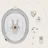 A baby bouncer with attached mobile toys, a charging cable, and a remote control, laid out against a plain background. Produktbild-Vorschau
