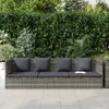 A gray rattan sofa with dark gray cushions sits on a light gray tiled patio, with a dense green hedge in the background. Podgląd zdjęcia produktu