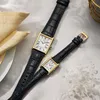 Two Seiko watches with black leather straps and gold-colored rectangular cases are displayed on a white textured surface. Podgląd zdjęcia produktu