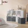 A white cube shelf unit with storage boxes, a pink handbag, and a floral arrangement, placed in a room with a bed and a rug. Produktbild-Vorschau