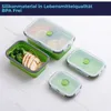 A set of green silicone food storage containers with clear lids, some filled with food, arranged on a light-colored surface. Produktbild-Vorschau