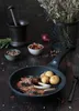 A rustic food photography scene featuring a frying pan with lamb chops and potatoes, surrounded by ingredients and kitchen tools. Produktbild-Vorschau