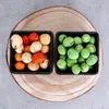 Two black square bowls filled with snacks, placed on a wooden surface. Voir les images du produit