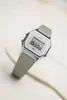 A digital watch with a gray strap is placed on a textured surface. Produktbild-Vorschau