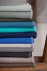 A stack of folded blankets in various shades of blue and gray. Produktbild-Vorschau
