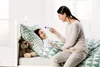 A woman is taking a child's temperature with a thermometer while the child is lying in bed. Produktbild-Vorschau