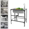 A stainless steel sink with a faucet and vegetables inside, supported by a black metal frame. The image also includes a collage of other kitchen equipment. Podgląd zdjęcia produktu