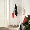 A white coat rack with a black coat and a red shopping bag hanging on it, placed next to a door and a bench with pillows. Produktbild-Vorschau