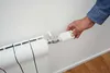 A hand is adjusting a smart thermostat on a radiator. Produktbild-Vorschau