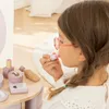 A young girl is playing with a toy makeup set, applying lipstick. Podgląd zdjęcia produktu
