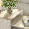 A close-up shot of a modern living room setting, featuring a travertine coffee table with a vase of white flowers and a book. Produktbild-Vorschau