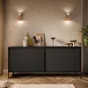 A modern living room with a black sideboard, artwork, and wall sconces. Produktbild-Vorschau