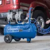 A blue air compressor is shown in front of a red vehicle, with a coiled blue hose extending towards the vehicle's tire. Produktbild-Vorschau