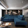 A modern living room with a large blue sectional sofa as the focal point, set against a dark stone wall with built-in shelving. Produktbild-Vorschau