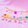 Two gold charm bracelets with various colorful beads and charms laid out on a pink textured surface. Podgląd zdjęcia produktu