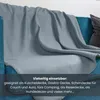 A gray fleece blanket draped over a blue sofa. Produktbild-Vorschau