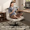 A woman is sitting in a white office chair, reading a magazine. The chair is in a home office setting with a desk and shelves in the background. Produktbild-Vorschau