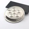 A stainless steel escargot dish with six compartments is placed on a white surface, with a black rectangular slate behind it. Produktbild-Vorschau