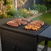 A barbecue grill with various meats and skewers cooking on it, set in a garden. Podgląd zdjęcia produktu